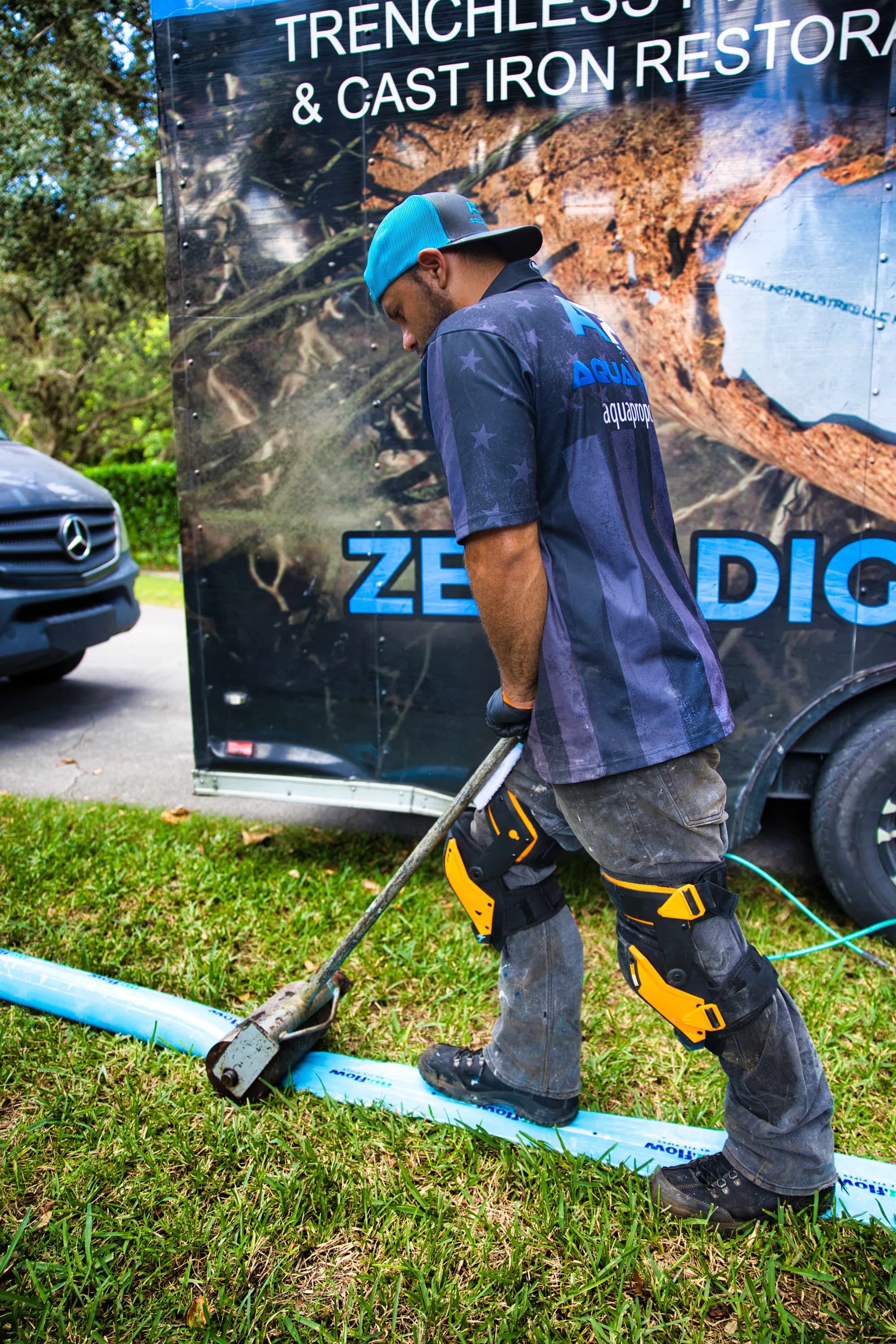 An Aqua Pro technician rolling a blue liner on the lawn beside the company trailer