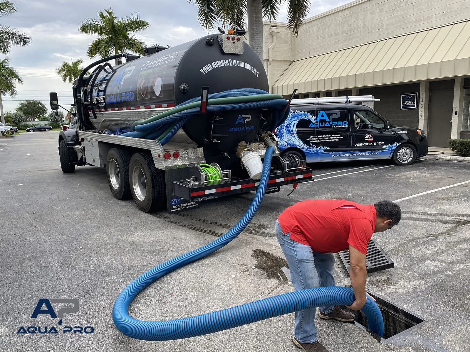 An Aqua Pro crew member handling a vacuum hose at a paved access opening beside the company truck