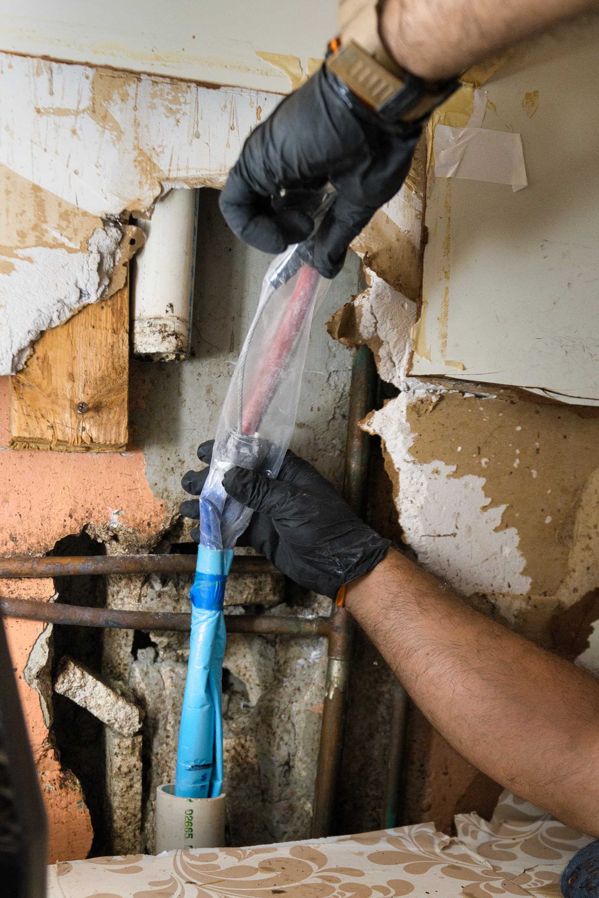 Gloved hands guiding equipment into a pipe access point