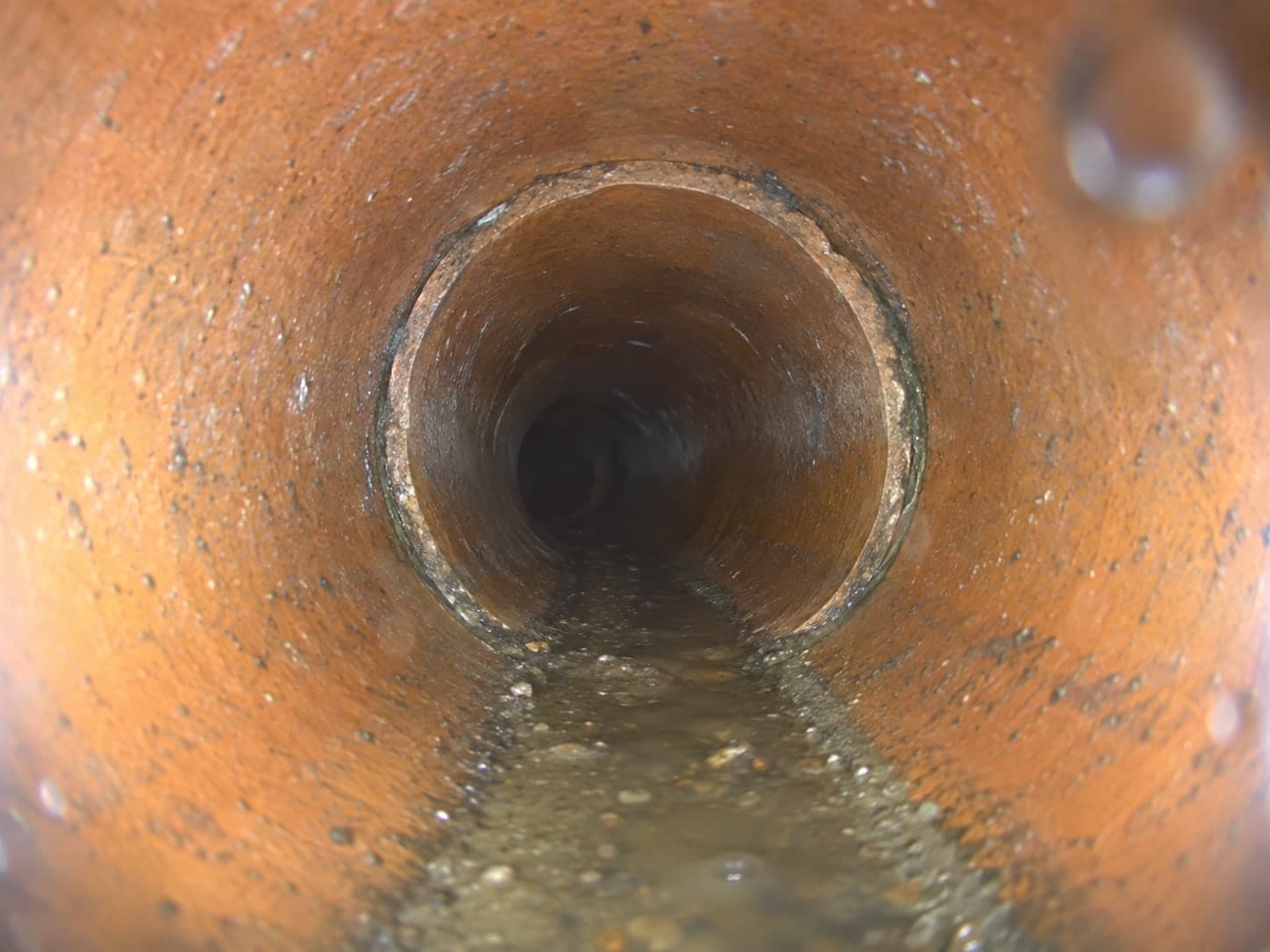 Illustration: camera footage of a clay pipe joint with a fogged lens and water on the pipe floor