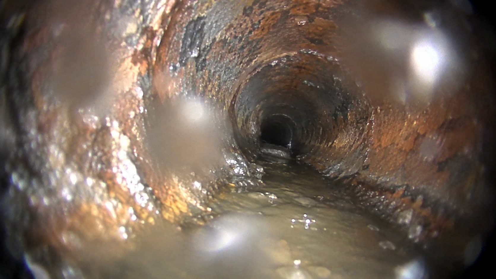 Illustration: camera footage inside a corroded cast iron sewer line with water droplets on the lens