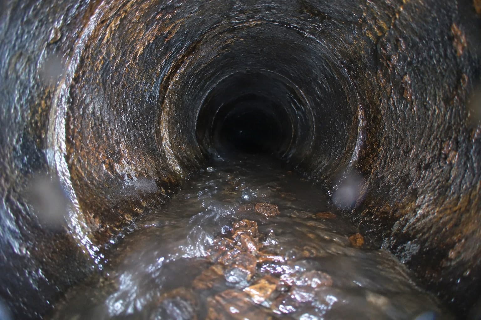 Illustration: loosened rust scale being flushed out of a cleaned cast iron pipe