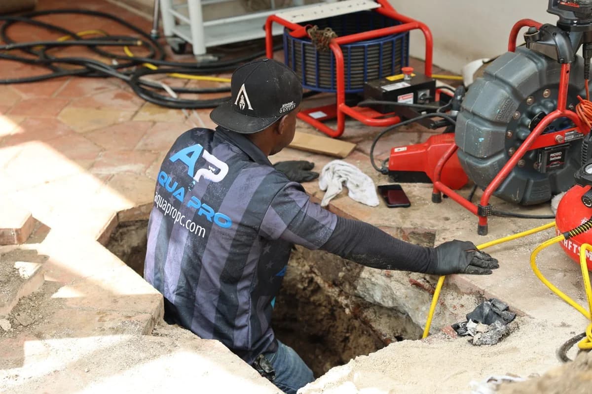 An Aqua Pro technician at an open floor access with a pipe inspection camera and monitor